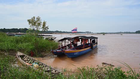 Touring-Boats-on-Mekong-River-moored-safely-as-flood-muddy-water-moves-down-the-river-while-Thai-flags-flying-as-seen-in-the-afternoon-in-Sam-Pan-Bok-in-Ubon-Ratchathani,-Thailand