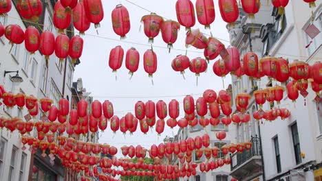 Stunning-Chinese-lanterns-in-Chinatown-London,-swaying-in-the-wind-with-birds-flying-overhead-on-an-overcast-day