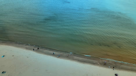 Aerial-view-of-the-shoreline-of-Baltic-Sea-while-people-walking-along-the-beach