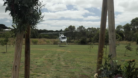 Helicóptero-Aterriza-En-Un-Campo-Visto-A-Través-De-Un-Cenador-De-Bodas,-Cámara-Lenta