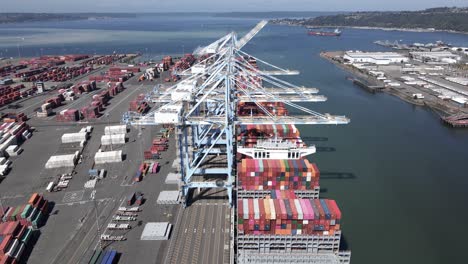 Giant-cranes-unload-multicolored-containers-from-the-decks-of-container-ships,-aerial-flyover