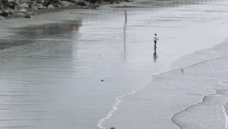 Eine-Einsame-Person,-Die-An-Einem-Kalten-Tag-Den-Strand-Hinaufspaziert,-Während-Die-Wellen-An-Land-Rollen