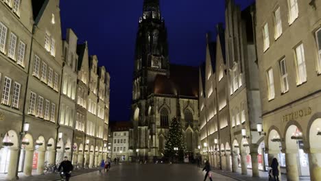 Tilt-up-shot-of-beautiful-lighting-city-buildings-and-famous-high-rise-St-Lambert's-Church-in-background-during-evening