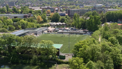 Toma-Aérea-De-Maidstone-Fc,-Elevándose-Sobre-Los-árboles-Para-Revelar-A-Los-Jugadores-De-Fútbol-Entrenando-En-El-Campo