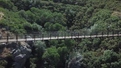 Drone-Shot-following-an-active-man-running-on-an-outdoor-hanging-suspension-bridge-above-Bear-Canyon-in-Draper-City,-Utah