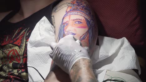 Tattooer-making-tattoo-of-girl-face-on-man-arm,-using-his-tattoo-machine,-cleaning-white-skin