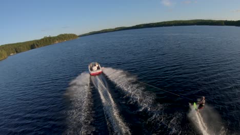 Zeitlupe---Slalom-Wasserski-Des-Weißen-Mannes-Vom-Weißen-Boot-Auf-Blauem-See-Im-Sommersonnenunterganglicht,-Fpv-Drohne-Luftspur-Folgen