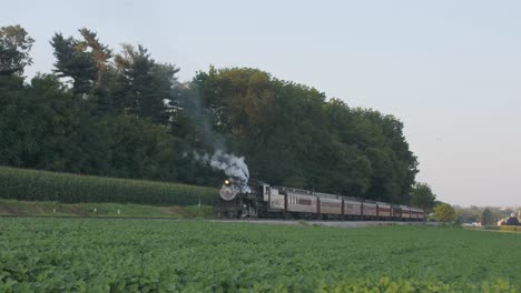 Una-Máquina-De-Vapor-De-1924-Con-Un-Tren-De-Pasajeros-Que-Echa-Humo-Y-Viaja-A-Lo-Largo-De-La-Campiña-Amish-En-Un-Día-De-Verano