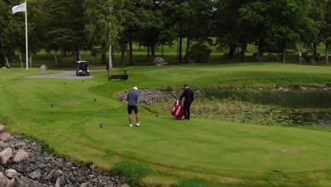 El-Golfista-Se-Balancea-Y-Golpea-La-Pelota-En-El-Campo-De-Golf-Junto-Al-Lago,-Tiro-De-Arco