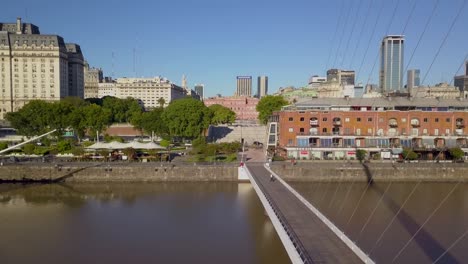 Aerial-flying-alongside-Woman’s-Bridge-with-Libertador-Building-and-Casa-Rosada-on-background