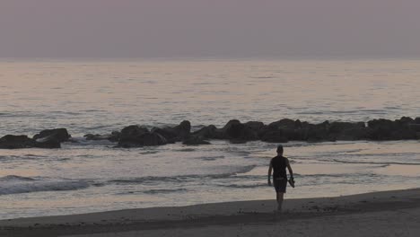 Man-walking-on-beach-barefoot-at-dawn,-slow-motion-silhouette