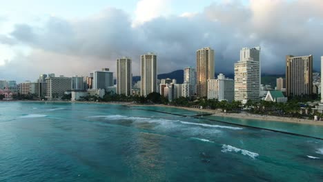 Toma-Panorámica-De-La-Playa-De-Waikiki-En-Un-Día-Tormentoso-Tropical,-Olas-Rodando-Mientras-Los-Surfistas-Esperan