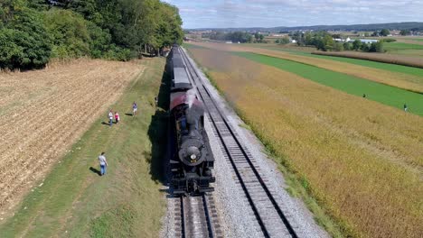 Aerial-View-of-the-Front-of-a-Antique-Steam-Engine-Stopped-at-Station-with-Antique-Passenger-Cars-Through-Amish-Farm-Lands-on-a-Sunny-Autumn-Day-as-Seen-by-a-Drone