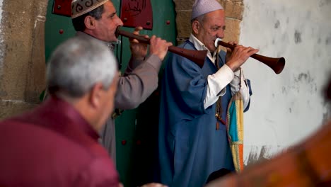 Shot-through-group-of-men-playing-drums,-closeup-of-two-men-playing-rhaita-or-mizmars-during-a-Sufi-trance-ceremony-in-Essaouira,-Morocco