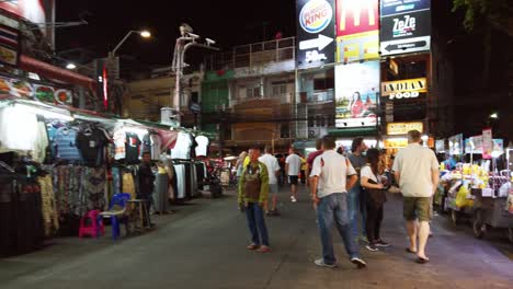 Handheld-scenes-of-the-tourists-are-walking-around-Khao-San-Road-at-night-time-famous-which-each-year-tourists-from-many-countries-came-to-visit-in-Bangkok,-Thailand