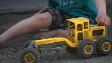 Kleiner-Junge-Spielt-Mit-Einem-Spielzeug-Grader-LKW-Im-Dreck