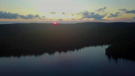 Aerial-watching-the-sun-go-below-the-horizon-over-a-calm,-scenic-lake
