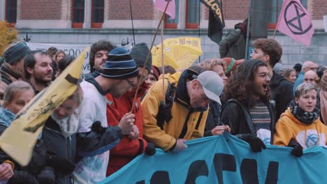 Junge-Extionction-Rebellion-Aktivisten-Und-Umweltschützer-Bilden-Eine-Menschliche-Mauer,-Während-Sie-Während-Des-Protestes-Gegen-Den-Klimawandel-In-Amsterdam,-Niederlande,-Banner-Und-Fahnen-Halten