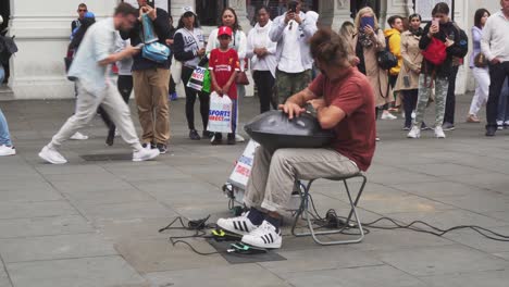 Busker-playing-hand-drum-music-on-London-street-in-front-of-people-around
