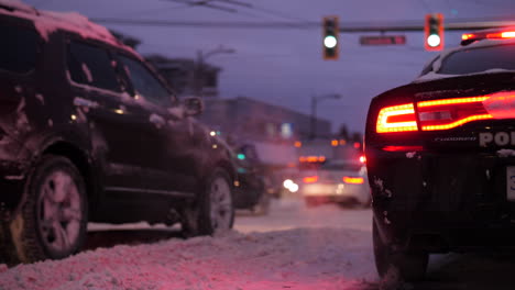Snowy-City-Road-and-Police-Car-with-Lights-on-while-Cars-drive-by-in-slow-motion