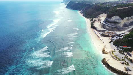 Blauer-Ozean-Und-Weiße-Wellen,-Die-über-Ruhige-Türkisfarbene-Lagunen-Rollen,-Die-Sandstrand-Zwischen-Felsiger-Küste-Der-Tropischen-Insel-In-Bali-Waschen