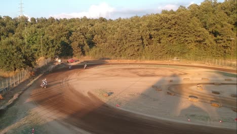 Motocross-that-drift-on-a-curve-of-a-dirt-track-circuit,-high-view