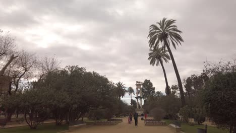People-walking-through-garden-park-on-cloudy-day-in-Seville,-Spain