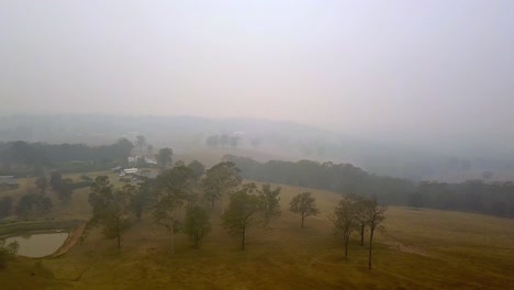 Homes-in-fire-danger-from-nearby-eucalyptus-tree-forest-blaze-with-heavy-smoke,-Aerial-drone-left-pan-shot