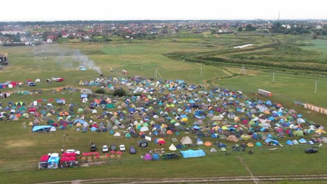 Vista-Aérea-De-Carpas-Multicolores-Colocadas-En-Un-Campo-En-Un-Festival-De-Música-Con-La-Ciudad-En-Segundo-Plano