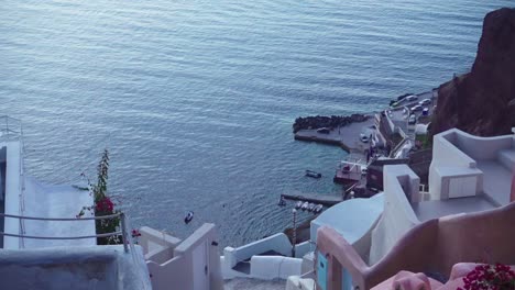 Edificios-Rosas-Y-Blancos-De-Santorini-Desde-Un-ángulo-Alto-Con-Barcos-En-Un-Muelle-En-El-Fondo