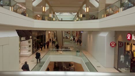 Mirando-Por-Encima-De-Una-Baranda-En-Niveles-En-Un-Gran-Centro-Comercial-Con-Vidrio-Y-Cromo-Y-Compradores-Caminando-Dentro