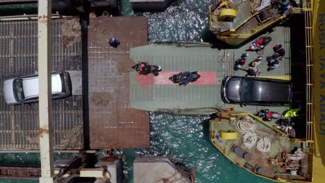 Nusa-Jaya-Abadi-vehicle-ferry-at-Port-Roro-offloading-cars,-people-and-mopeds-coming-from-Bali,-Aerial-top-view-rising-shot