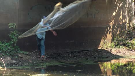 Wide-Exterior-Static-Shot-of-a-Man-With-Helmet-Throwing-Fishing-Net-on-the-Lake-in-the-Day