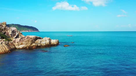 Peaceful-seascape-with-blue-azure-sea-under-bright-sky-with-white-clouds-on-rocky-coastline-of-tropical-island