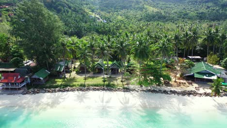 Beach-cabins-and-bungalows-with-sea-view-built-on-quiet-shore-of-tropical-island-under-palm-trees-on-tropical-island-in-Thailand