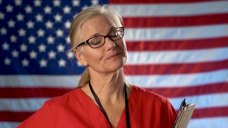 Portrait-of-a-nurse-walking-from-US-flag-to-foreground-and-showing-a-smile-and-approval