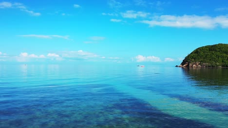 Bright-blue-sky-with-beautiful-white-clouds-reflecting-on-glassy-calm-sea-surface-near-shore-of-tropical-island