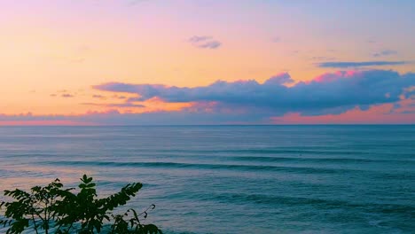 HD-Hawaii-Kauai-slow-motion-static-wide-shot-over-a-tree-in-lower-left-and-ocean-with-beautiful-reddish-orange-cloudy-sky-near-sunset
