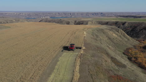 Cosecha-Combinada-Roja-Grande-En-El-Borde-De-Un-Gran-Campo-De-Colza-Con-Amplias-Vistas-Expansivas-Sobre-Un-Río-Distante