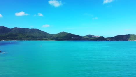 Vivid-colors-of-beautiful-shoreline-of-tropical-island-with-green-hills-under-bright-blue-sky-with-white-clouds-reflecting-on-turquoise-lagoon-in-Philippines