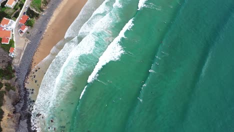 Surfers-seen-from-above-in-Praia-da-Arrifana-in-west-Portugal-Atlantic-coast,-Aerial-top-view-lowering-shot