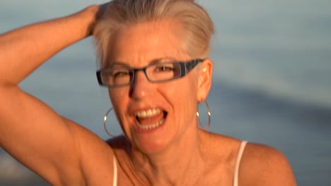 Closeup-of-mature-blonde-woman-with-gray-hair-playing-with-her-hair-and-looking-old-in-granny-glasses-and-laughing