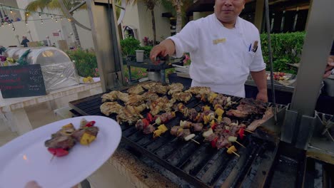 El-Chef-Mexicano-Adulto-Coloca-Shish-Kabobs-En-Un-Plato-De-Una-Persona-Caucásica-En-Un-Evento-Al-Aire-Libre