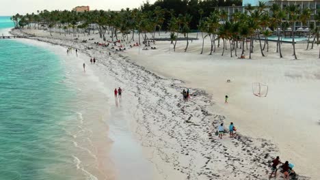 Aérea,-Playa-De-Arena-Blanca-Donde-Las-Parejas-Caminan-De-La-Mano-A-Lo-Largo-De-La-Orilla,-República-Dominicana