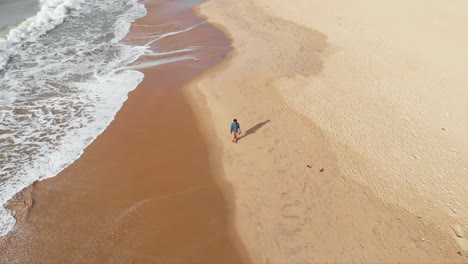 Top-down-Aerial-Follow-shot-of-a-27-year-old-young-Indian-male-walking-alone-in-the-seashore-by-himself-shot-with-a-drone-in-4k