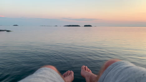 Man-hanging-his-legs-over-the-calm-sea-at-sunset