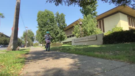 Young-Caucasian-children-cycling-along-sunny-CalTech-campus-building-sidewalk