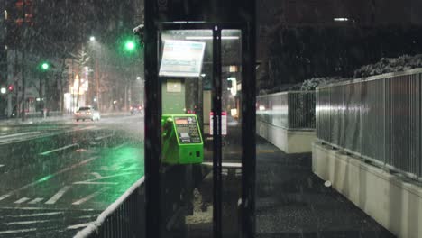 Cabina-Telefónica-En-La-Calle-De-La-Acera-Con-Autos-Que-Viajan-De-Noche-Durante-Una-Fuerte-Nevada-En-Kyoto,-Japón