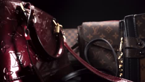 Vista-Macro-Volando-Más-Allá-De-Lujosas-Bolsas-De-Cuero,-Vintage-Y-Nuevos-Bolsos-Louis-Vuitton-En-Una-Escena-Oscura-Con-Fondo-Negro-Aislado,-Productos-Caros-Para-Los-Ricos