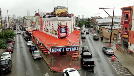Geno's-Steaks,-famous-with-tourists,-Philly-cheesesteak-restaurant,-aerial-with-Philadelphia-skyline-in-distance